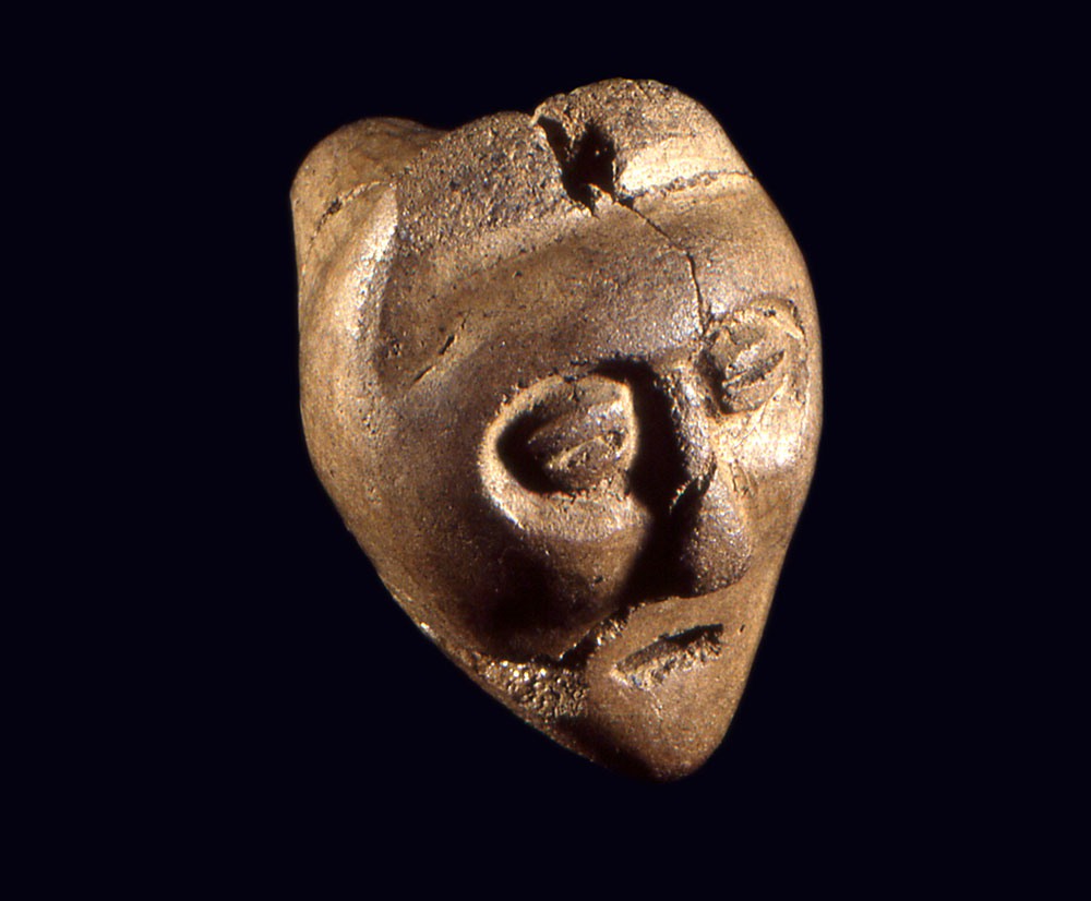 The human side of a double-headed effigy talisman recycled from a  14th-century ancestral Wendat pipe bowl found in Barrie, Ontario.  The other side is a representation of a wolf or dog-like head with  erect ears and a pointed snout.